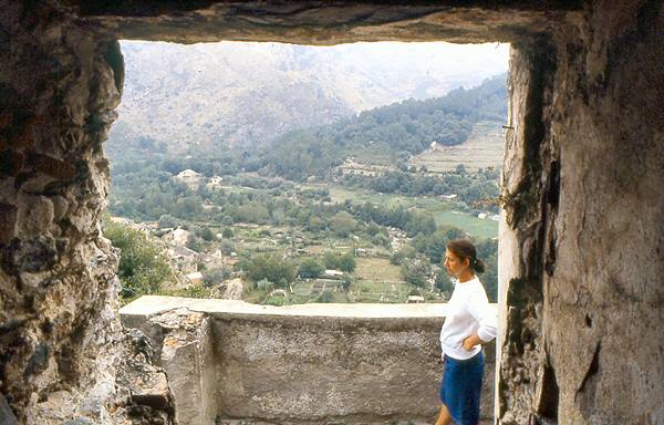 Woman in white shirt by rough stone window overlooking terraced valley and mountains