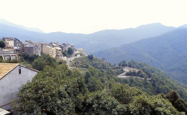 Stone village houses on green hillside, winding road descending between mountains