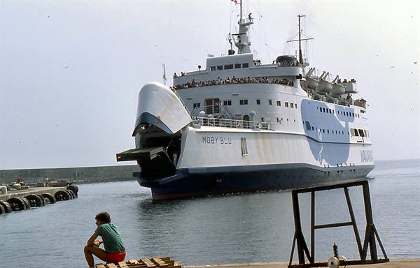 The ferry Moby Blu enters the harbor, a boy sitting on the dock watches
