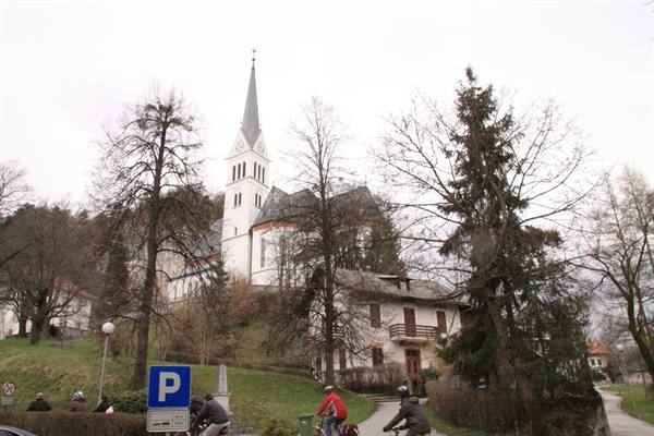 White church with steeple among bare trees, cyclists passing by