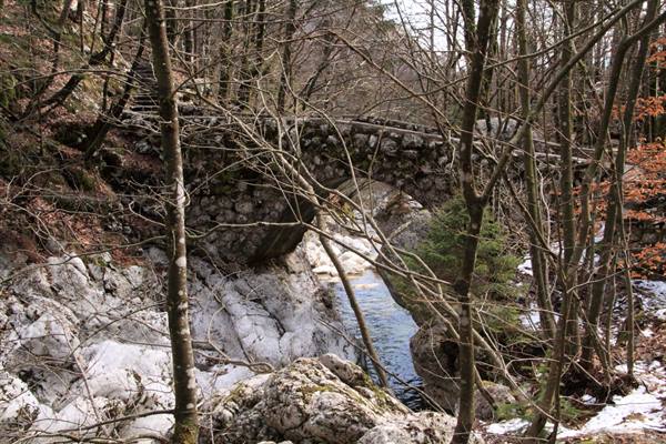 Stone bridge over a stream among white rocks and bare trees