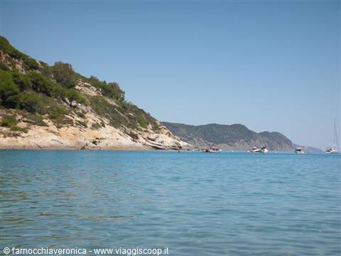 Turquoise water before green rocky hills, boats anchored along the coast