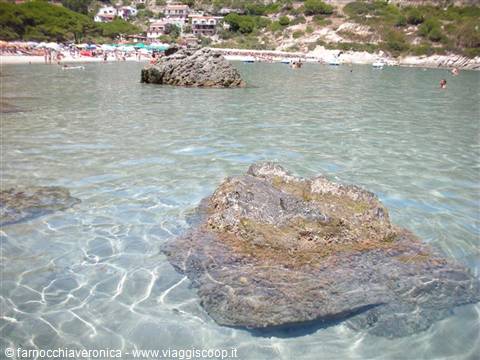 Rocks in clear water in front of the crowded beach at Baia dei Turchi