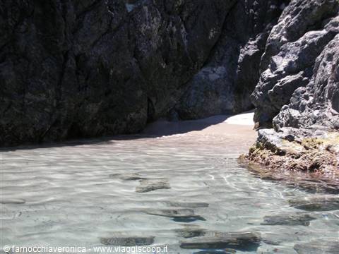 Clear water between dark volcanic rocks and a small sandy strip