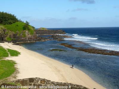 Pale sand beach with volcanic rocks and ocean waves, a person walking