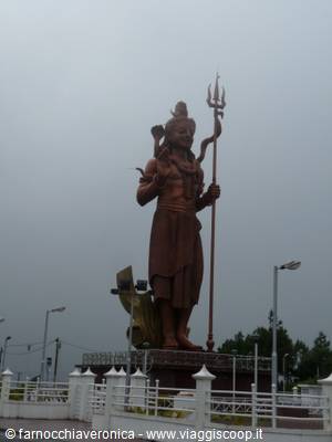 Bronze Shiva statue holding a trident, with Nandi behind, under grey sky