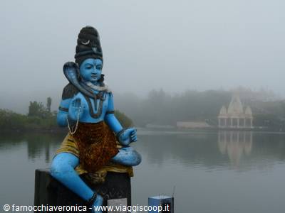 Blue Shiva statue on the foggy lake, white temple in the background