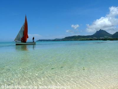 Red-sailed boat anchored in turquoise lagoon, green mountains in background