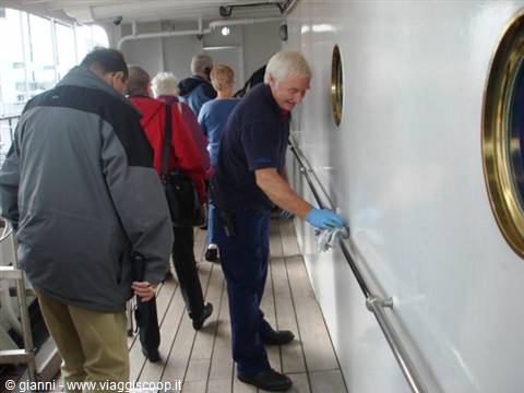 Sailor wipes the ship deck handrail, passengers in jackets nearby