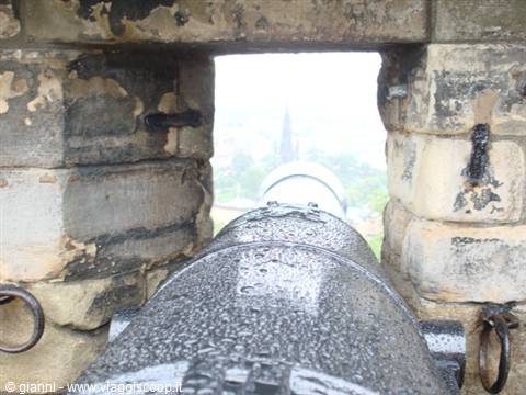 Rain-soaked black cannon on stone bastion aims out over the city
