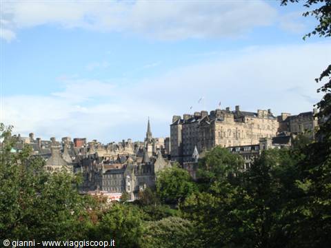 Historic stone buildings of Edinburgh among green trees, cloudy sky