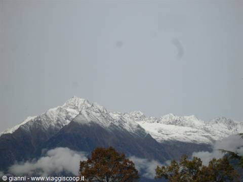 Snow-capped peaks emerging from clouds, autumn trees in the foreground
