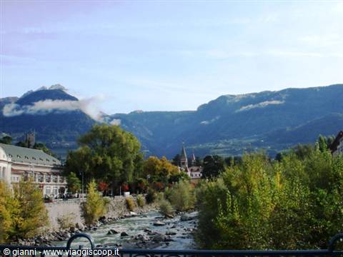 Merano: the Passer river flows between autumn trees and cloud-wreathed mountains