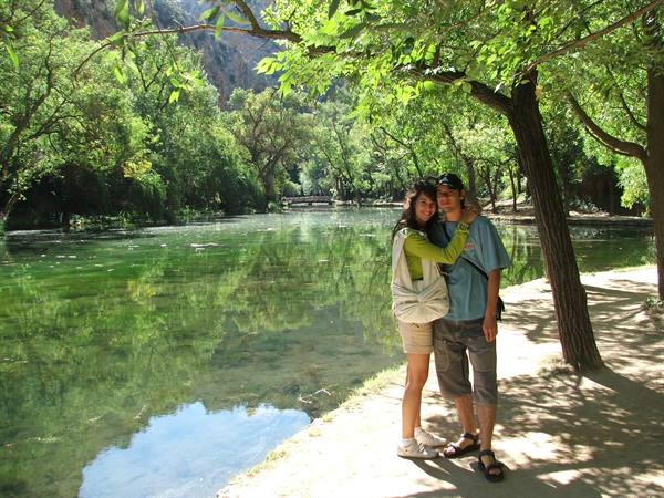 Couple hugging on sandy shore of a green pond surrounded by trees