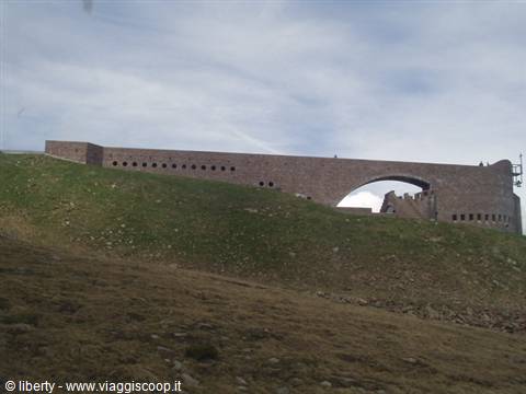 Modern stone chapel with large arch on grassy mountain slope