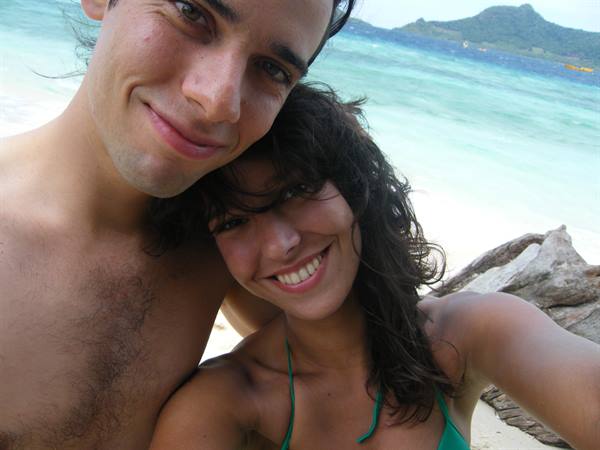Smiling couple selfie on white sand beach, turquoise sea and islands behind