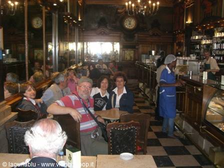 Tourists at a table in a historic café with clock and chandeliers