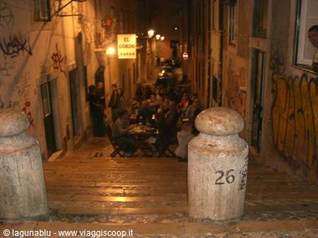 Steep alley with outdoor tables, graffiti walls and lit signs at night
