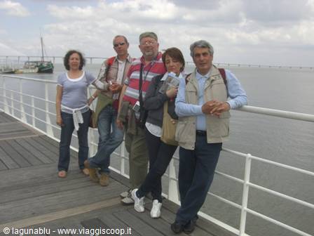 Five tourists posing on wooden boardwalk by lagoon with fishing boat