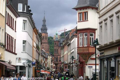 Crowded pedestrian street lined with colorful houses, red stone church tower, Heidelberg