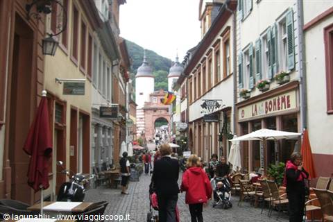 Pedestrians along a street with cafés and colorful houses toward the Heidelberg gate