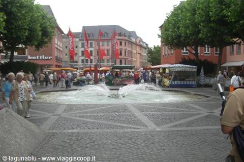 Town square with round fountain, market stalls and red flags among colorful buildings