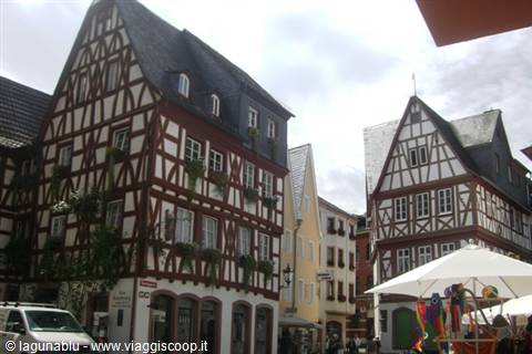 Half-timbered houses with flowers under grey sky, white umbrella market stall