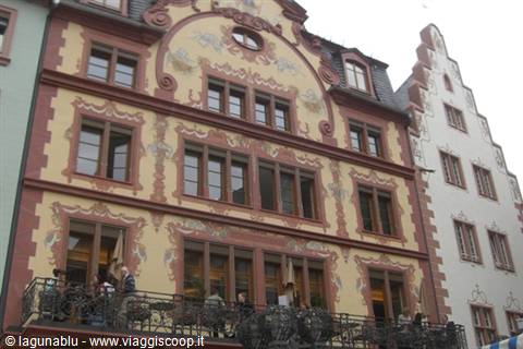 People under an ornate painted facade with iron balcony