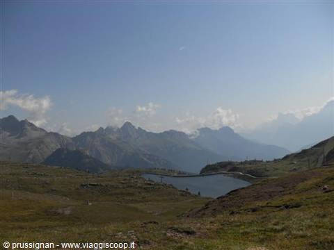 Alpine lake surrounded by grassy meadows and rocky peaks under cloudy sky