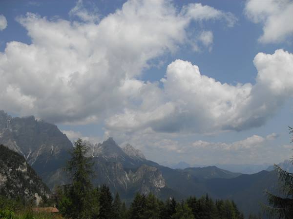 Rocky Dolomite peaks among fir trees, white clouds and blue summer sky
