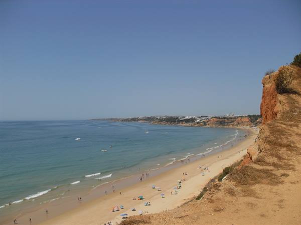 Sandy beach with swimmers and umbrellas beneath a reddish cliff, Algarve