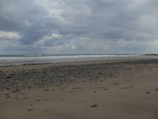 Sand and grey pebbles on beach, waves and stormy clouds over the ocean