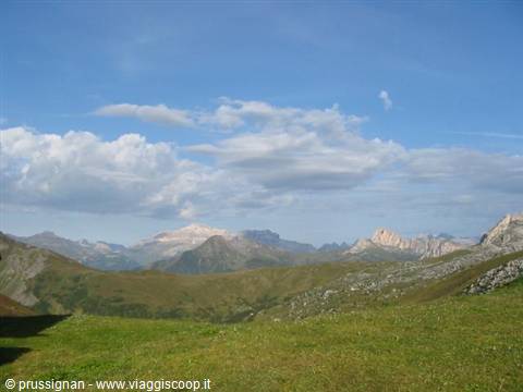 Green alpine meadows beneath rocky Dolomite peaks under white clouds