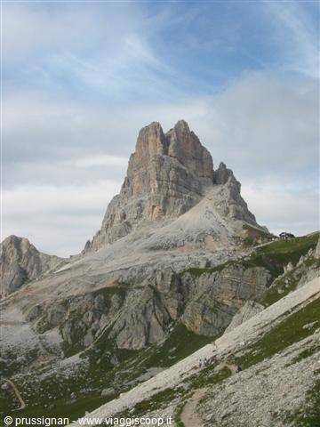 Rocky Dolomite spire under clouds, stony trails with hikers on the slope