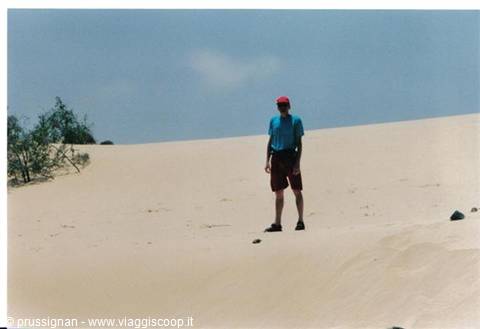 Tourist in red hat standing on a sandy dune, blue sky