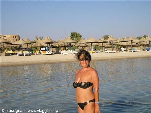 Woman in black bikini in the water, beach with straw umbrellas behind