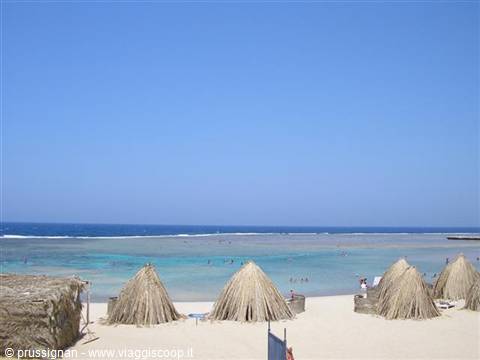Straw umbrellas on sandy beach in front of turquoise sea with swimmers
