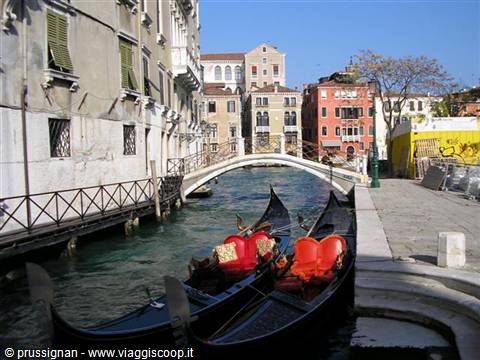 Black gondolas with red seats moored beside a small bridge in Venice