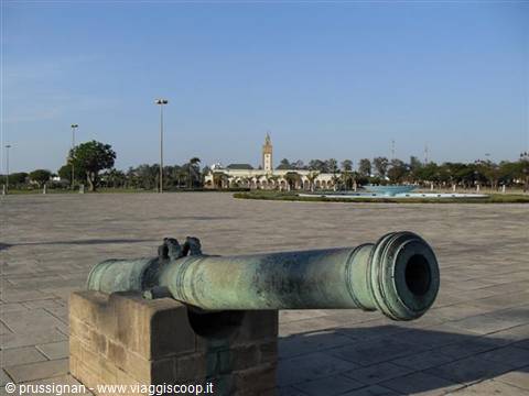 Bronze cannon on stone base, paved square and minaret in the background