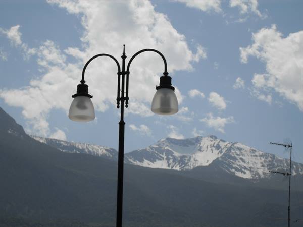Wrought-iron double street lamp against snowy mountains and cloudy sky