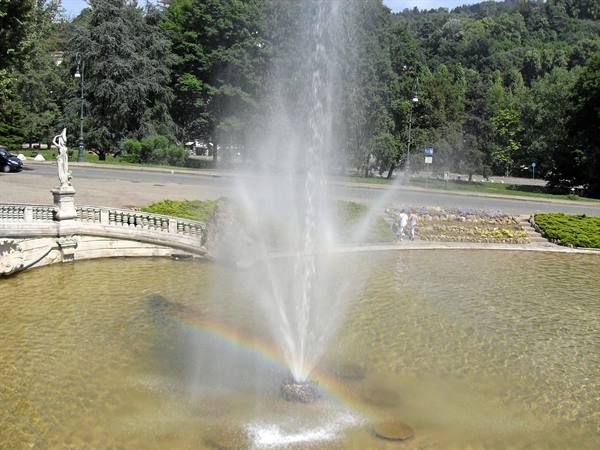 Fountain spraying water with a rainbow, statue on the stone balustrade