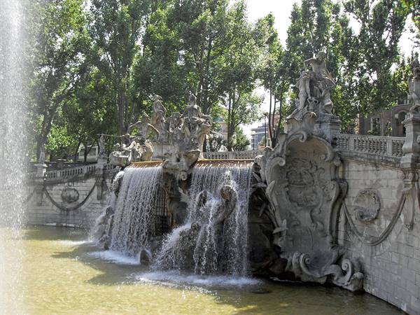 Baroque stone fountain with cascading water and statues among trees