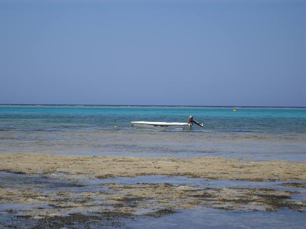 White boat stranded on shallow turquoise flat, man pushing it offshore