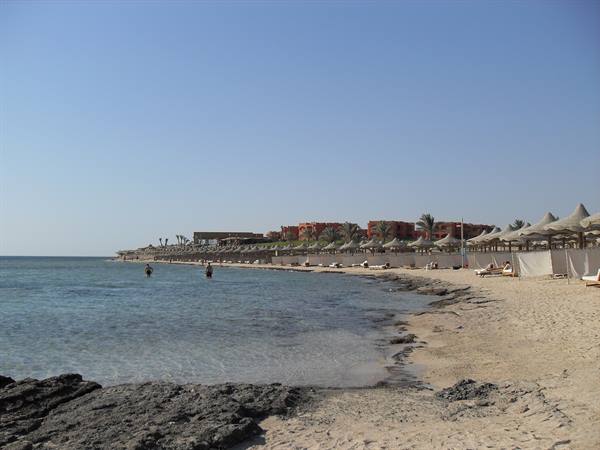 Sandy beach with straw umbrellas and rocky reef by the Red Sea