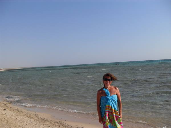 Woman in blue sarong and sunglasses on a sandy beach by the sea
