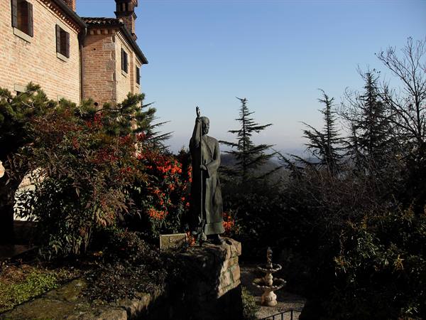 Bronze statue of a monk pointing skyward beside a brick building, red cone flowers