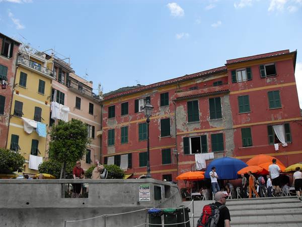 Colorful houses and orange and blue umbrellas, tourists strolling in Vernazza