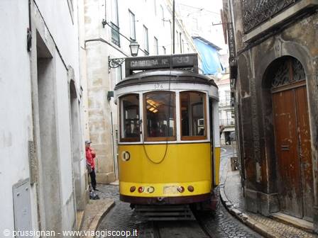Yellow vintage tram climbs a steep narrow street between old buildings in Lisbon