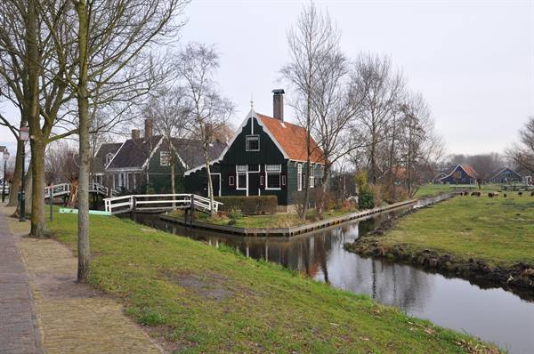 Green wooden house along a canal, white bridge and bare trees