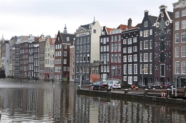 Amsterdam canal houses reflected in the water, cars parked along the quay